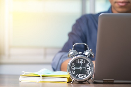 Male employee with clock and computer. Credit: https://www.istockphoto.com/portfolio/JaruekChairak