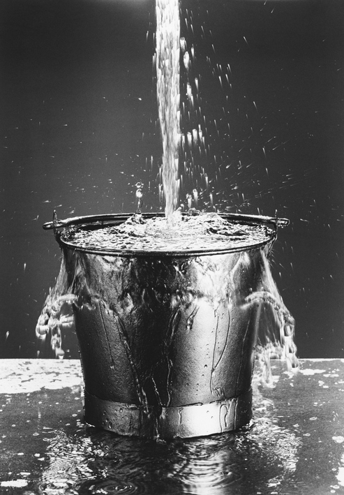 Black and white image of water pouring into overflowing bucket. Credit: https://www.istockphoto.com/portfolio/IPGGutenbergUKLtd